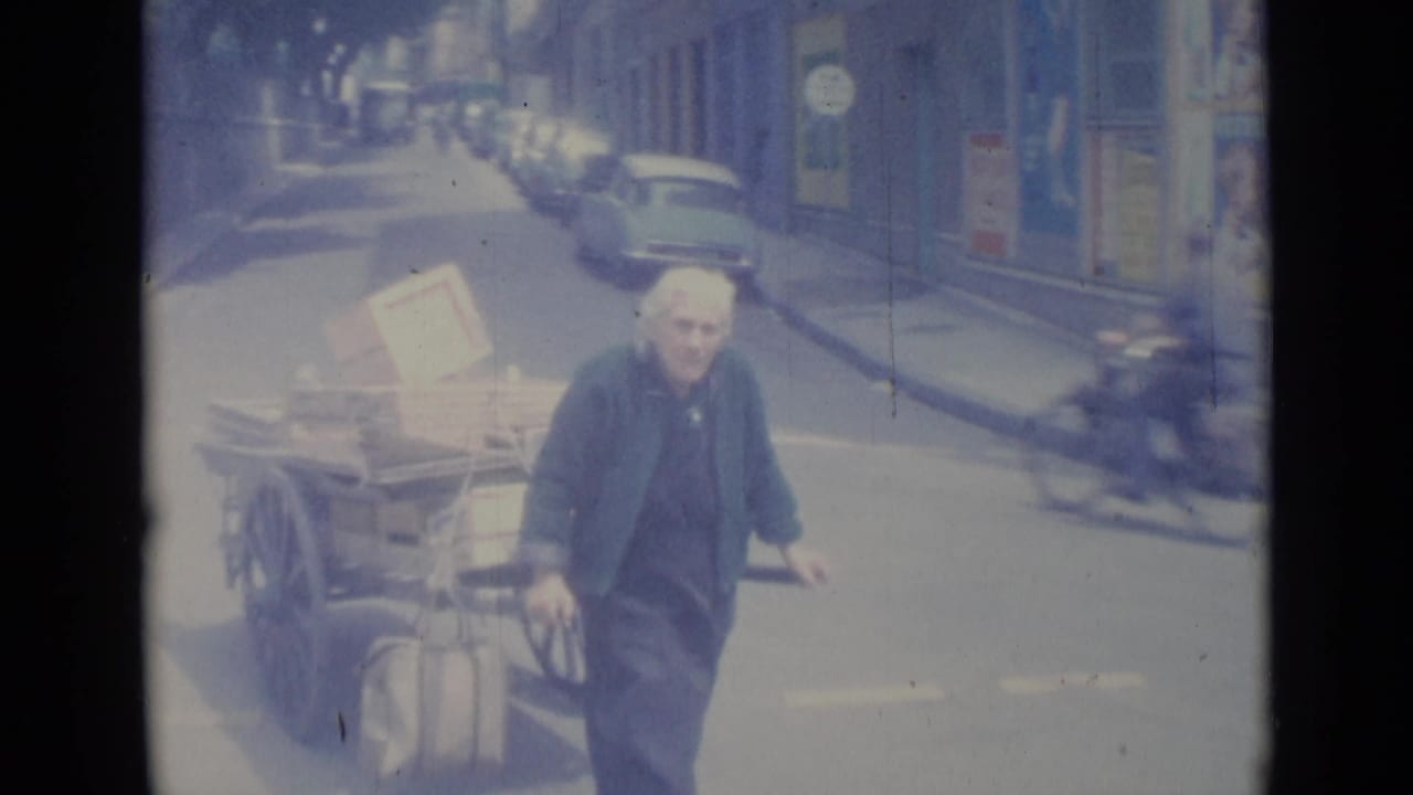 Older man pulling a loaded wooden cart along a city street.