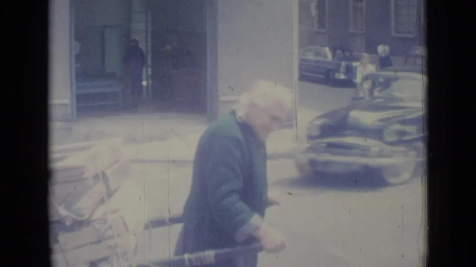 The older man and loaded cart move past a parked vintage car on a Nice street in 1962.