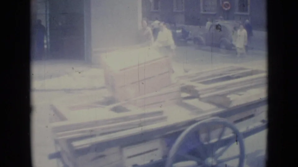 The cart and its wooden load fill the foreground while street steps, cars, and pedestrians remain visible through bright exposure.