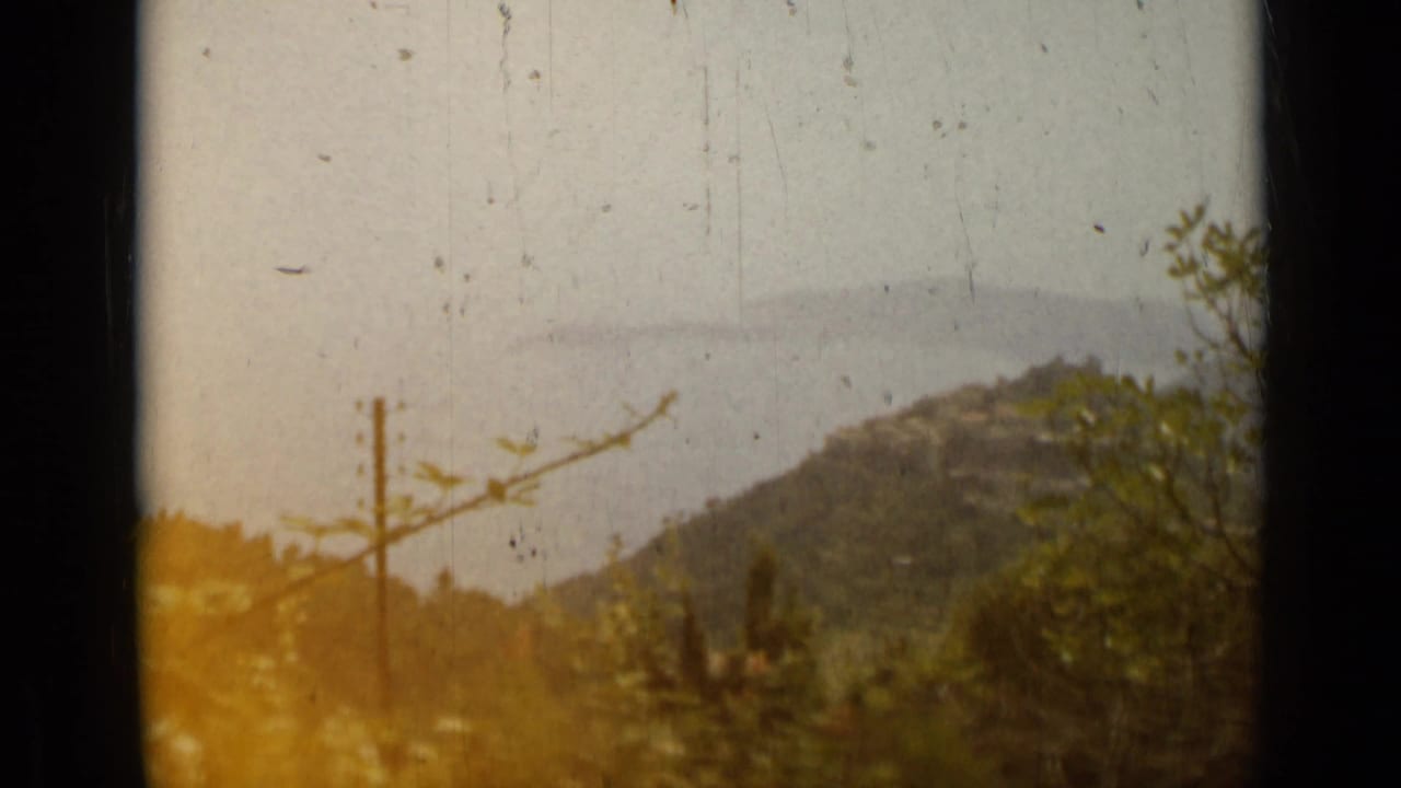 Hazy French Riviera hillside view near Nice, with trees, a utility pole, rolling terrain, and pale blue sea beyond.