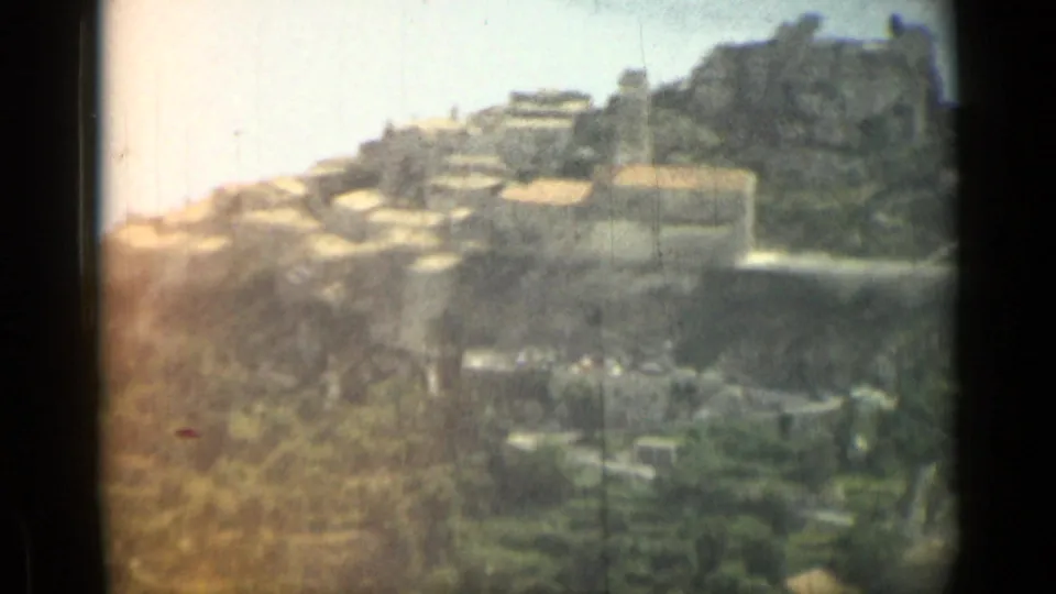 1962 8mm home-movie view near Nice, France, showing clustered hillside buildings, pale roofs, vegetation, and dark film gate edges.