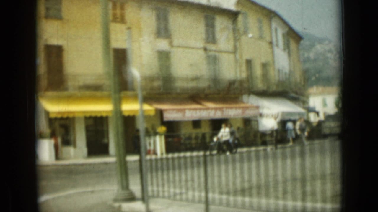 Nice street corner with yellow and red storefront awnings, pedestrians near the sidewalk, a motorcyclist, and pale upper-floor facades.