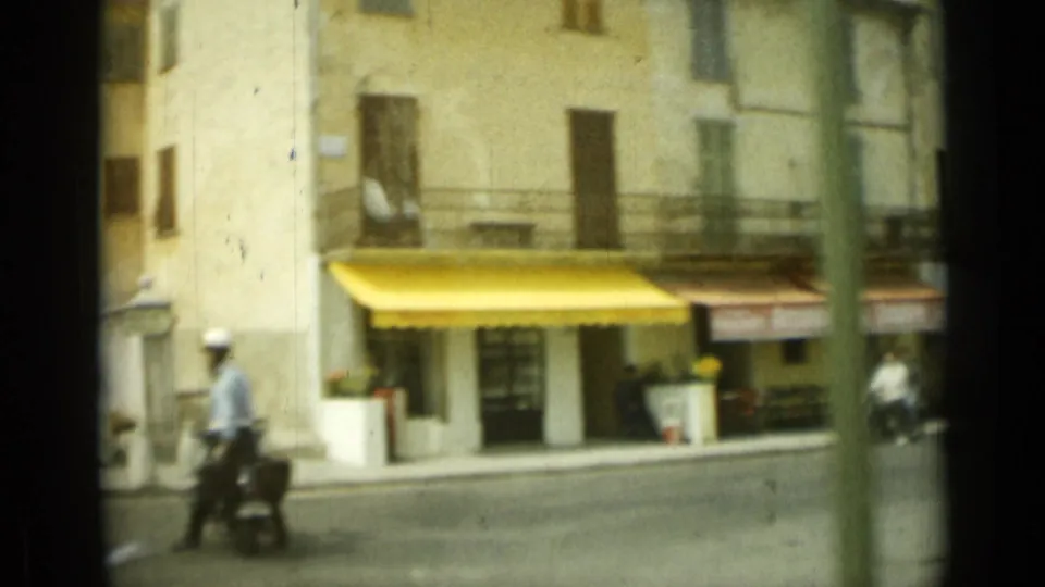 1962 Nice street view with pale facades, a bright yellow shop awning, and a scooter rider crossing the foreground.