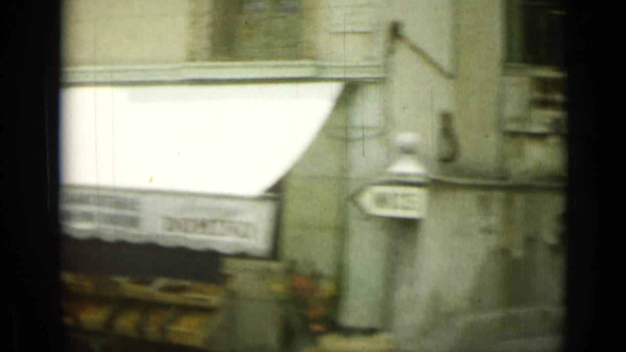 Passing 8mm view of a Nice street facade with a white awning, wall-mounted signs, and street fixtures.