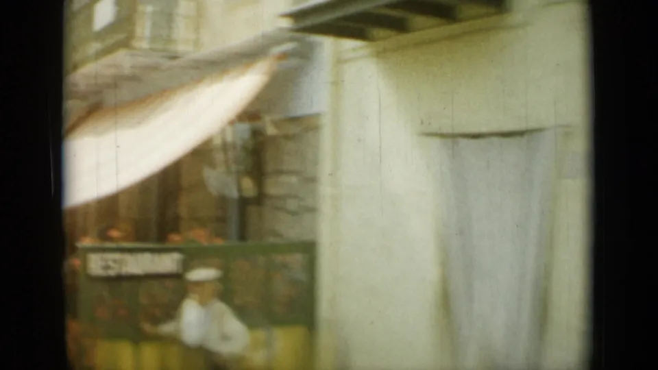 1962 Nice street view from moving 8mm footage, showing a striped awning, storefront sign, and soft, blurred street details.