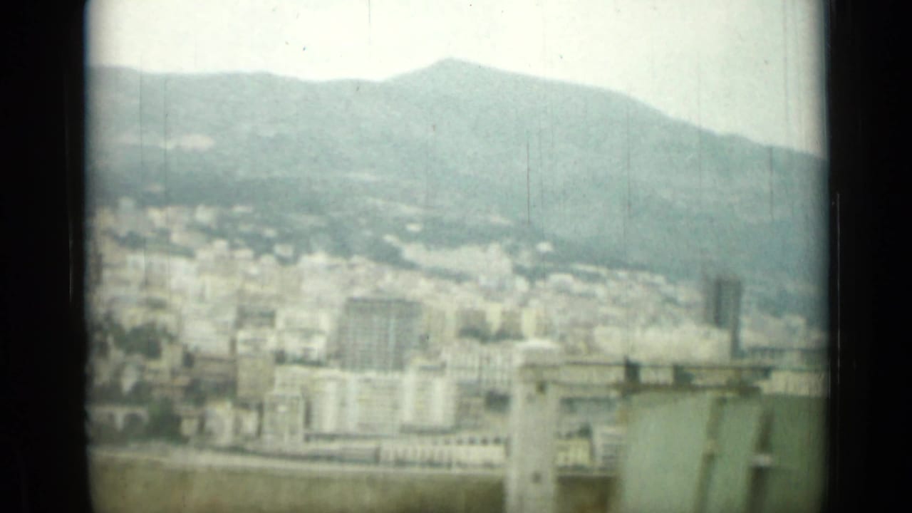 Soft elevated view of a hillside city with mountains in the background.