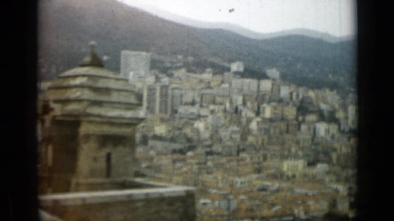 Elevated 8mm view in Nice, France, with a tower-like foreground structure, city buildings, and mountain slopes beyond.