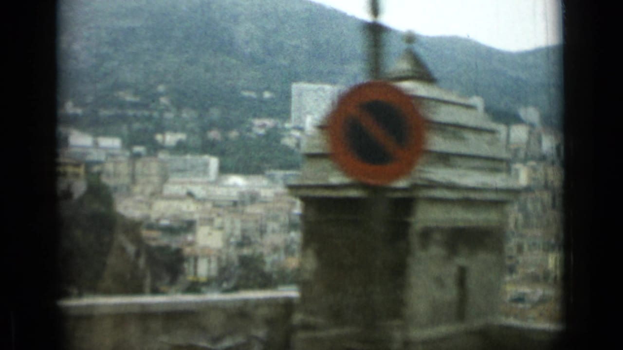 City buildings and mountains seen past a stone structure with a red no-parking sign.