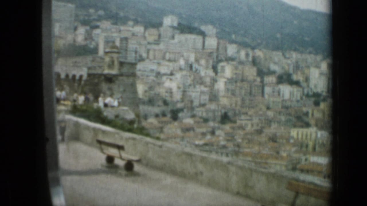 Nice, France overlook with stone parapet, wooden benches, and dense hillside buildings in the distance.