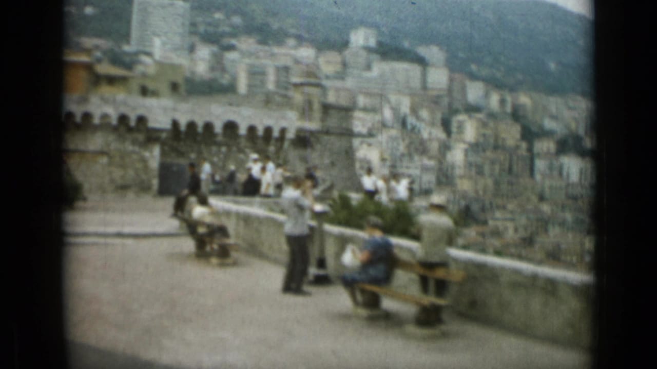 1962 Nice overlook scene with seated and standing tourists, benches, stone wall, and hillside city buildings.