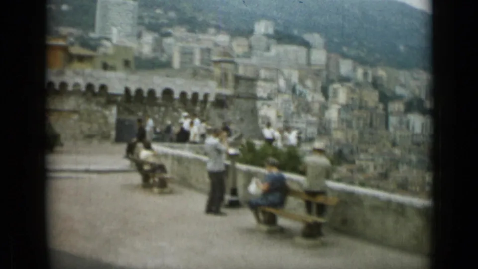 1962 Nice overlook scene with seated and standing tourists, benches, stone wall, and hillside city buildings.