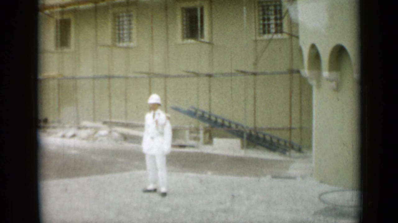 A uniformed guard or attendant stands in a paved area near a historic building, arched openings, steps, and barred windows in Nice.