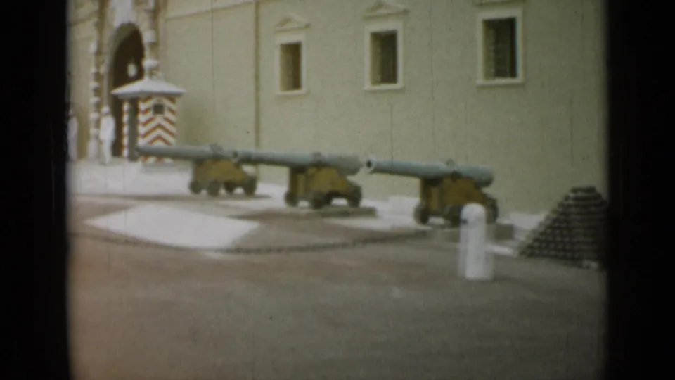 The frame shows mounted cannons, a striped guard box, and cannonballs outside a pale stone building in the 1962 Nice, France footage.