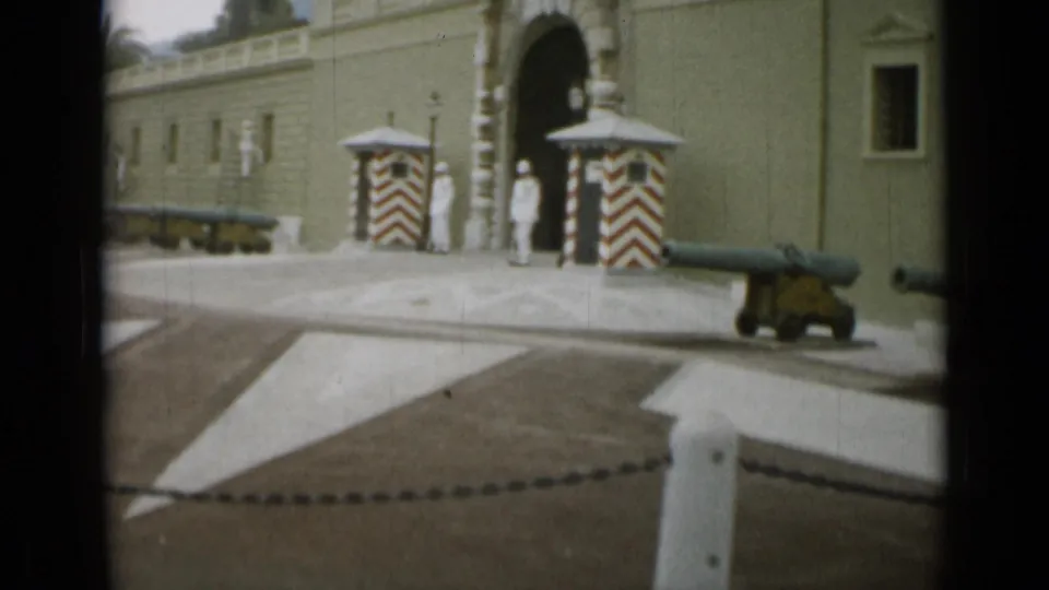 1962 Nice travel footage showing an ornate arched entrance with striped sentry boxes, cannons, and uniformed figures near the gate.
