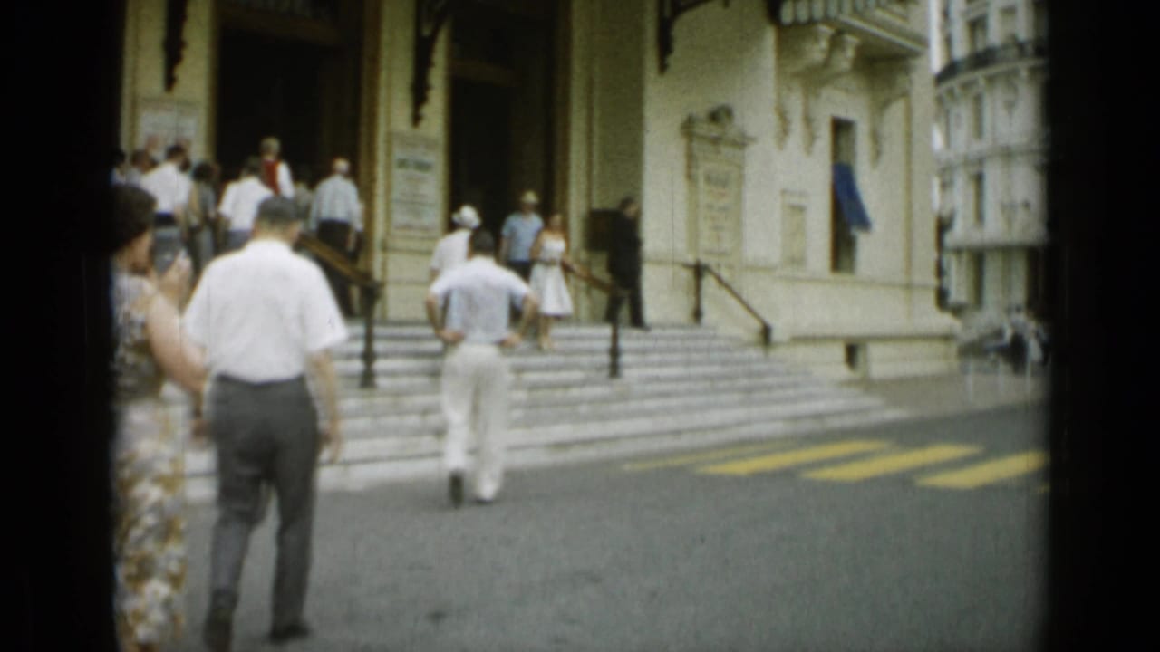 1962 Nice street-level view of adults in light clothing walking up broad steps toward an ornate building entrance.