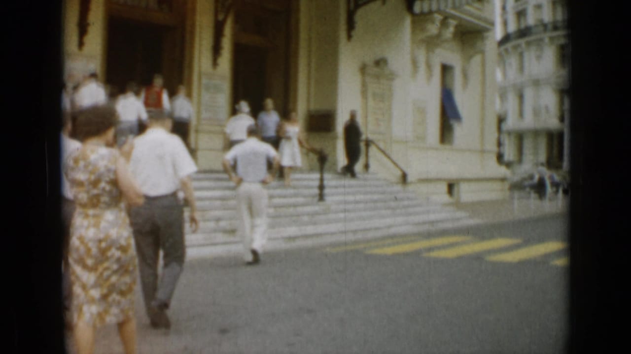 Adults walk across a street toward steps and a large building entrance.