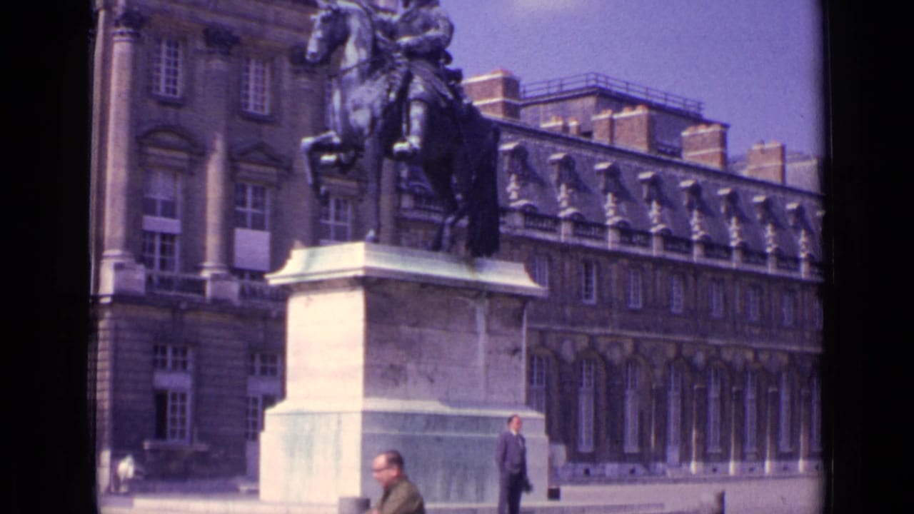 Equestrian statue on a stone pedestal before an ornate classical building, with pedestrians at the edge of the frame.