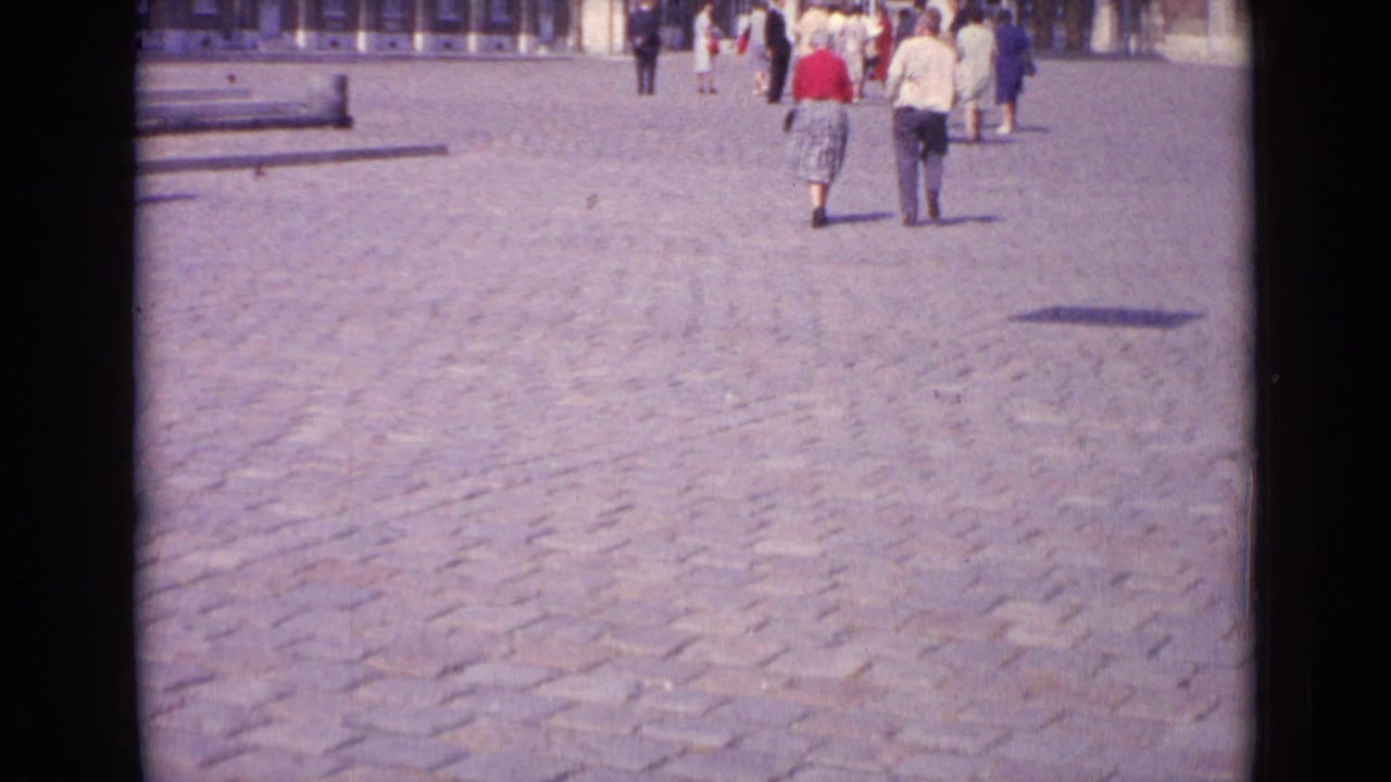 1962 Paris frame showing the statue and classical building beyond a cobblestone courtyard, with several visitors walking in mid-century dress.