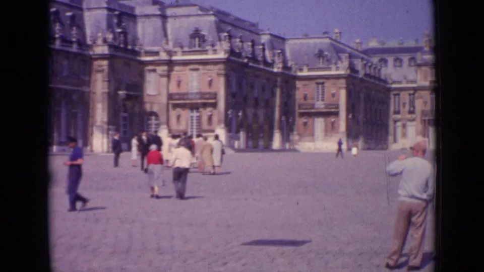 1962 Paris home-movie frame showing tourists in a sunlit plaza before grand classical buildings.