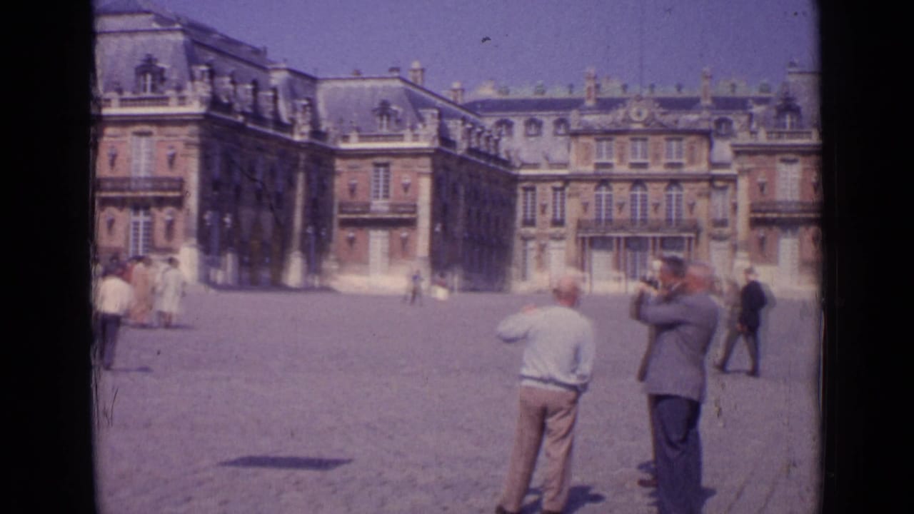 1962 Paris travel frame with tourists photographing and walking in a large classical plaza.
