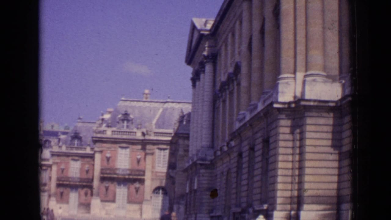 Vintage Paris frame with formal palace buildings, tall stone wall, roof dormers, and small figures near the courtyard edge.