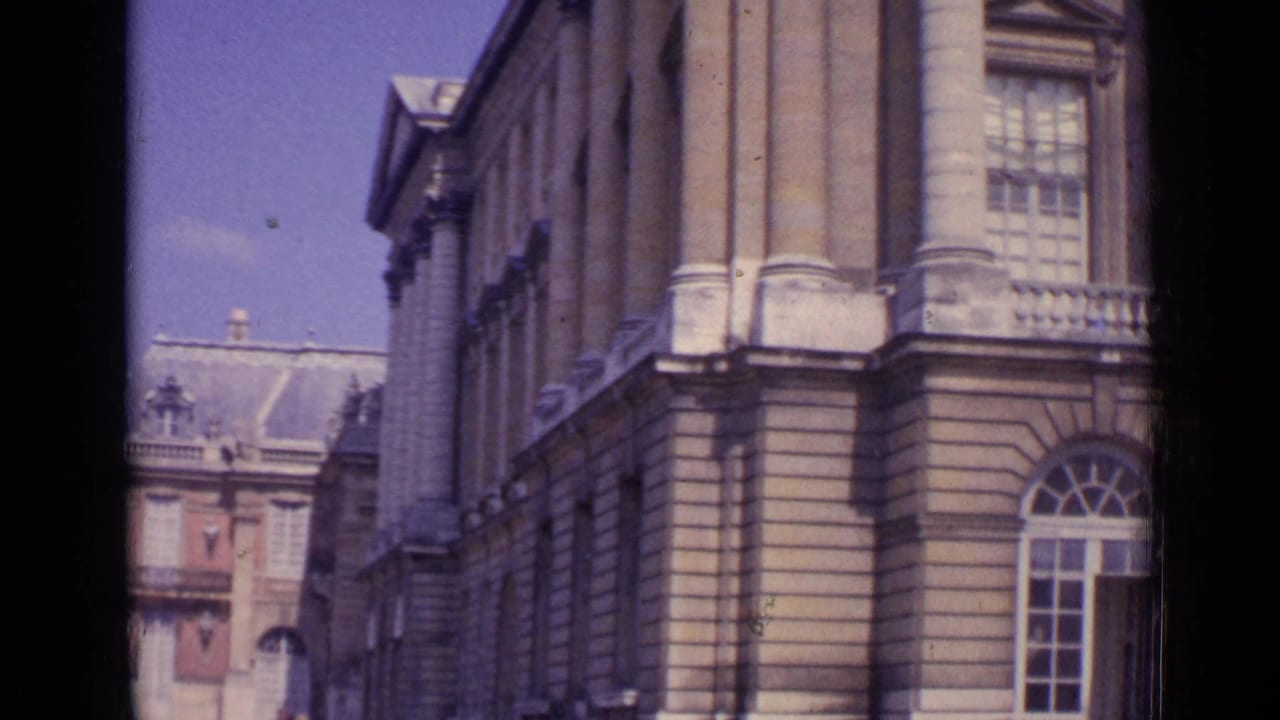 1962 Paris home-movie view of a palace side elevation with columns, arched windows, and a distant courtyard facade.