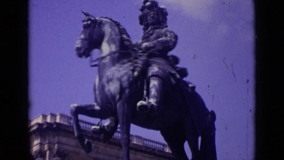 Low-angle 1962 Paris home-movie view of an equestrian statue beside a stone building, with dark film gate edges visible.