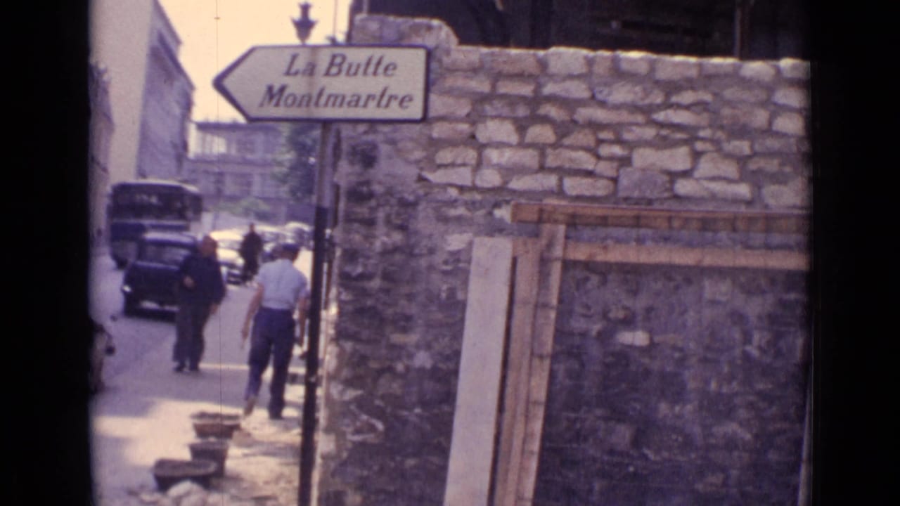 Paris street corner with a La Butte Montmartre directional sign, stone wall, pedestrians, and mid-century cars in the background.