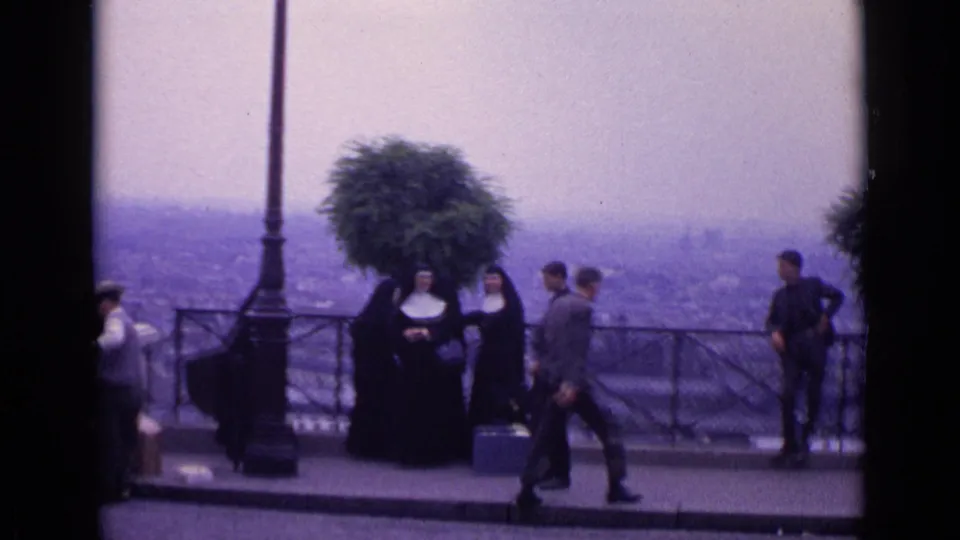 1962 Paris 8mm frame showing nuns and visitors in mid-century clothing at a hazy overlook, with a lamppost and railing in view.