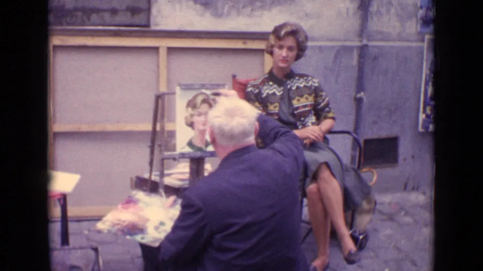 A Paris street portrait scene shows an adult painter facing a seated woman in a patterned sweater, with a portrait canvas between them.