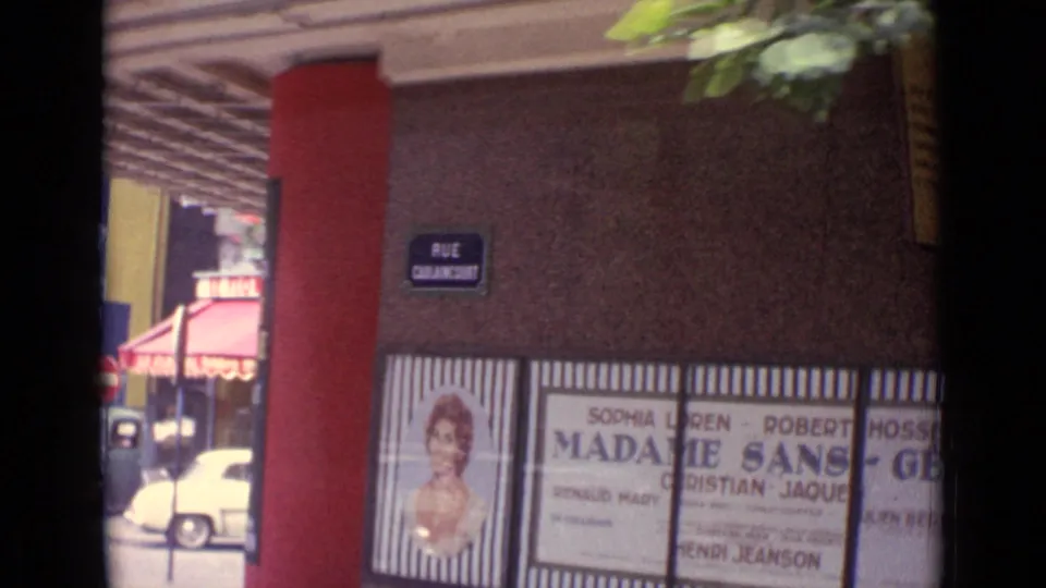 Paris street facade with a Rue Caulaincourt sign, red vertical trim, awning, and Madame Sans-Gene poster panels.
