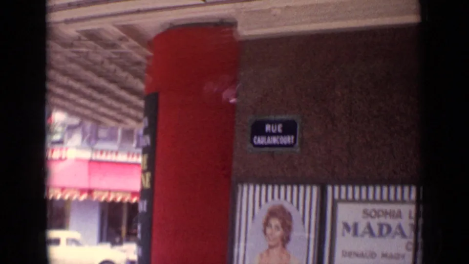 1962 Paris frame centered on a Rue Caulaincourt street sign, red facade edge, striped poster panels, and a partially visible car.