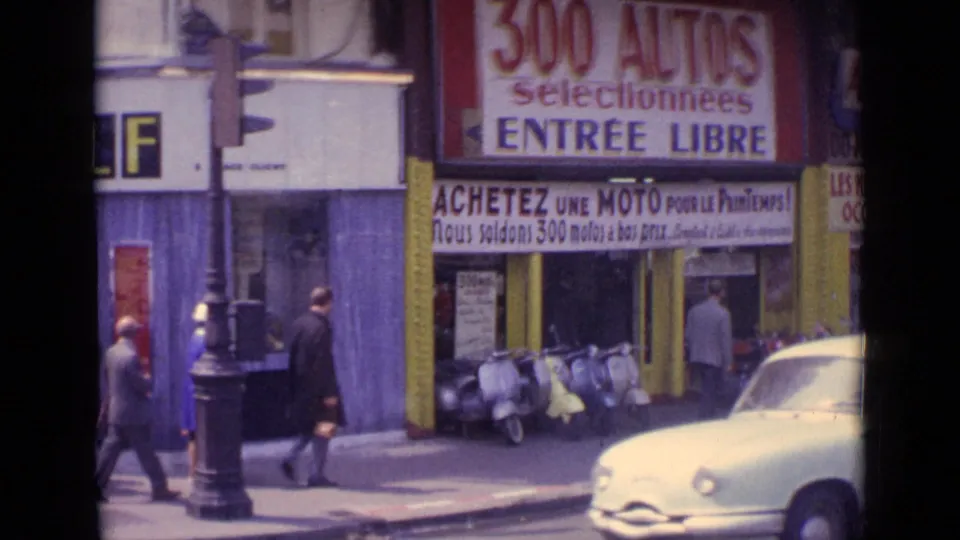 Paris street corner with pedestrians, parked scooters, a passing car, and bold French vehicle sales signage.