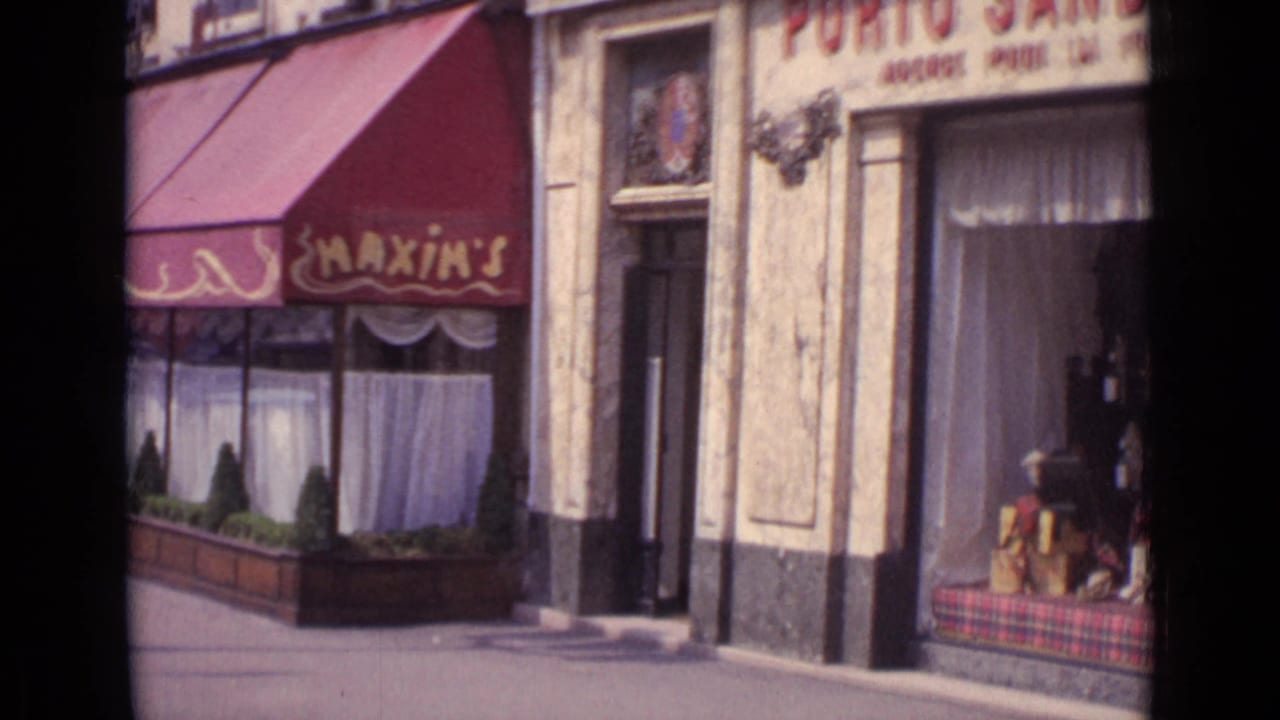 Paris storefront with red Maxim's awning, curtained windows, planters, and adjacent entrance.