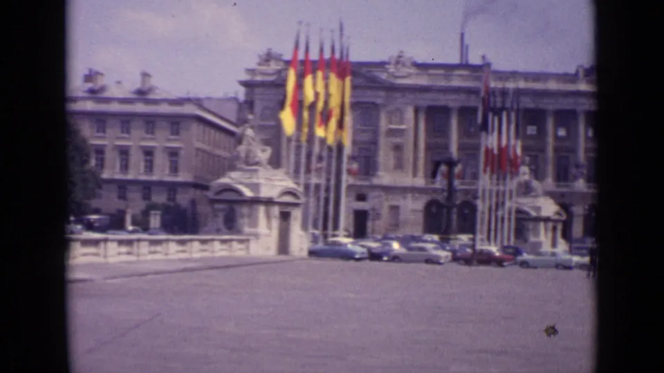 1962 Paris footage shows tall flags, a stone balustrade, parked cars and part of a formal urban building.
