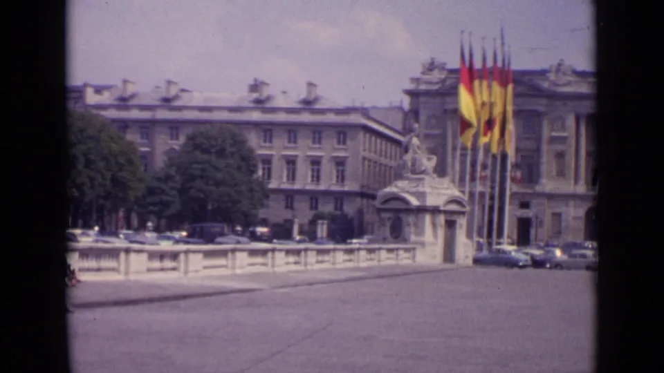A 1962 Paris travel-film frame shows a stone railing, trees, flags and a classical facade bordering the square.