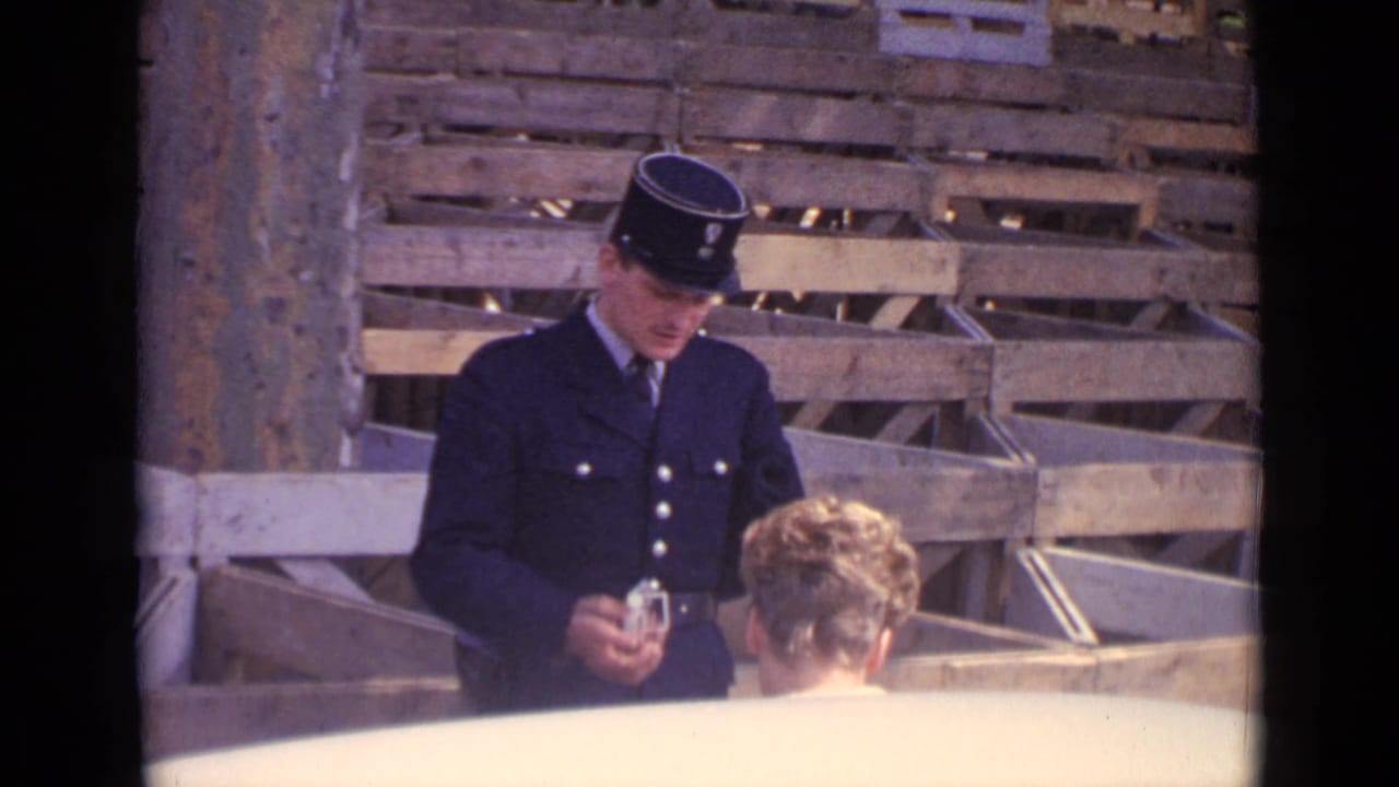 The 1962 Paris home-movie frame shows the policeman looking down at a small object while the woman listens.