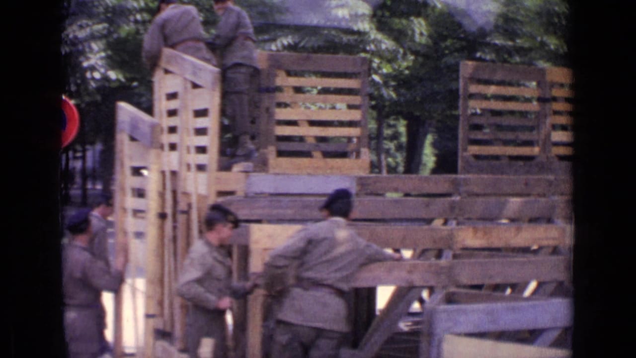 1962 Paris street view with soldiers in grey fatigues moving tall wooden barricade panels beneath trees.