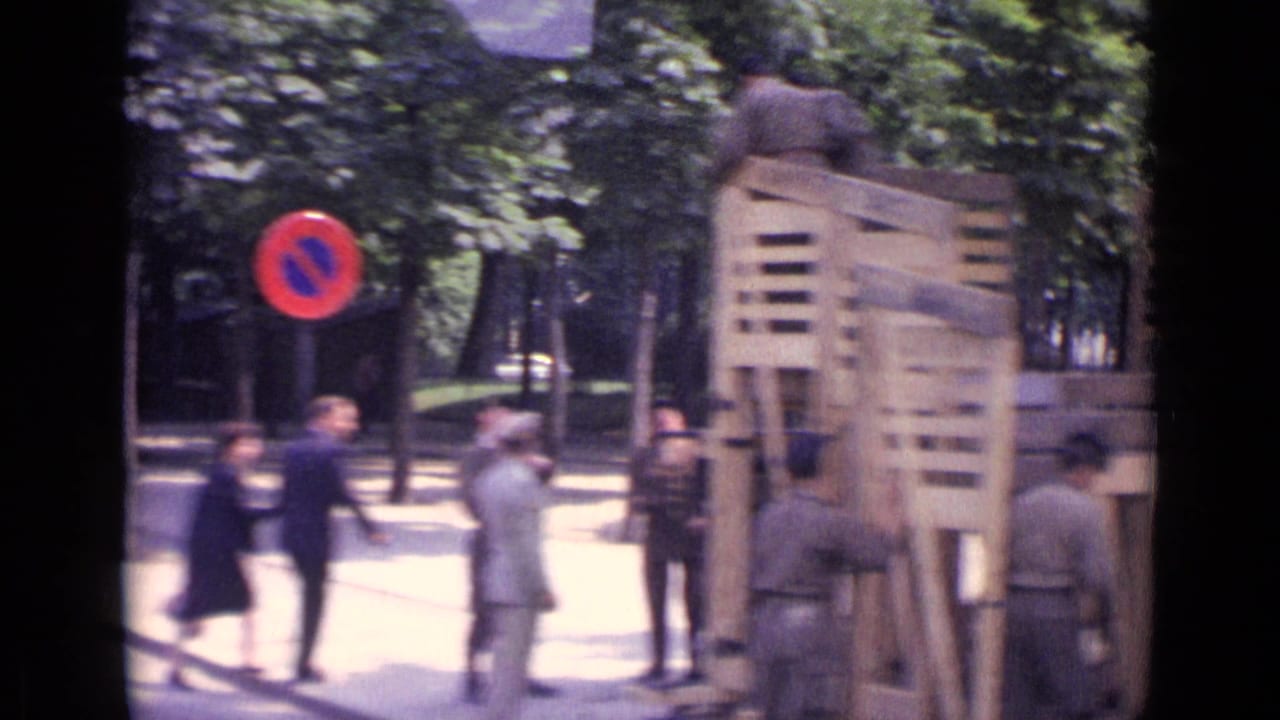 1962 Paris frame with soldiers around a wooden barricade, pedestrians nearby, and a red-and-blue no-parking sign at the curb.