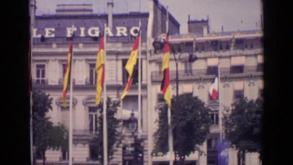 1962 Paris street view of the Le Figaro facade with French and German flags displayed on flagpoles outside.