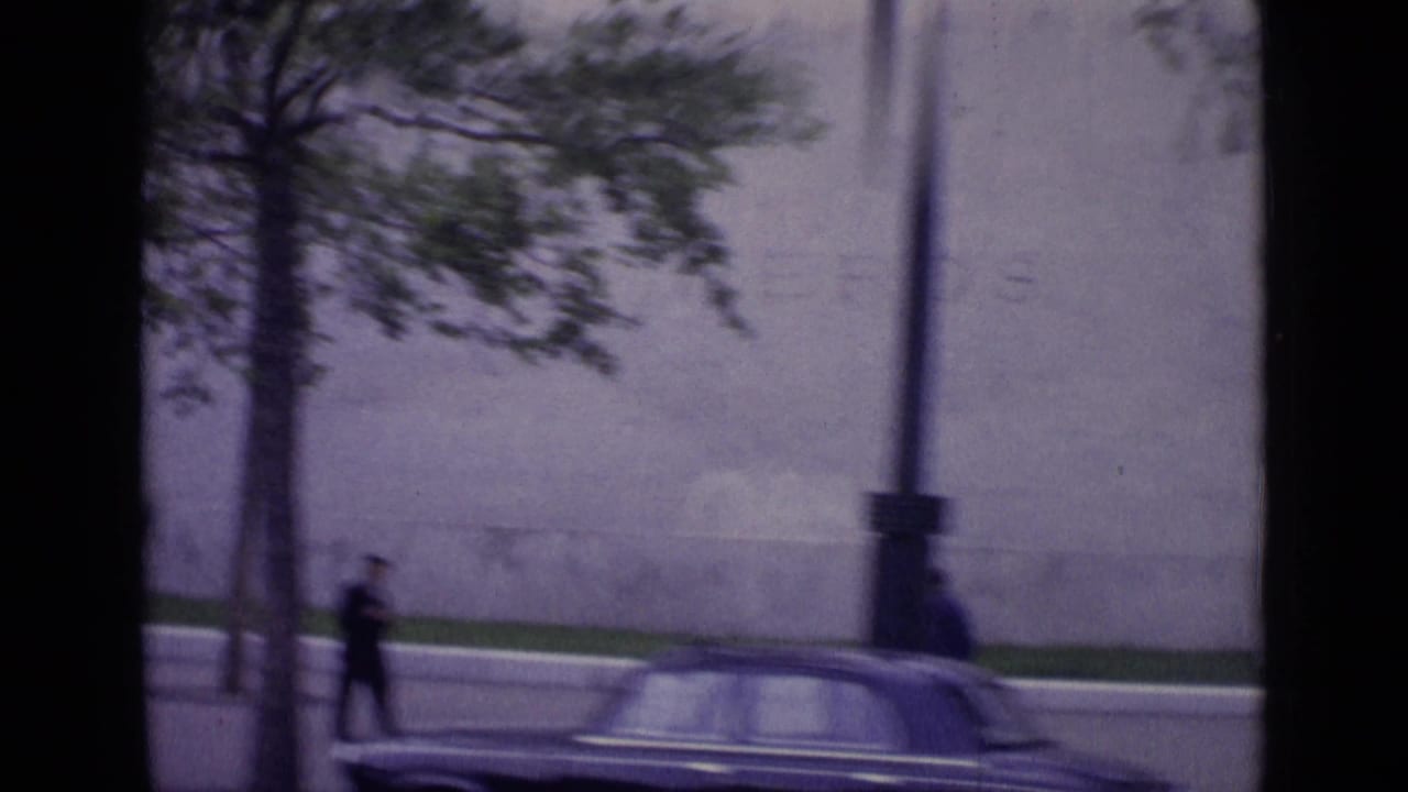 Street-level view from a car with trees, a classic automobile, pedestrians, and the Eiffel Tower partly visible.