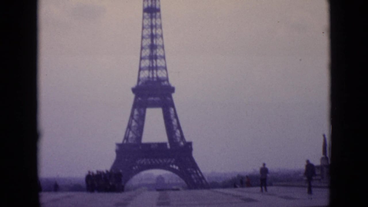1962 Paris frame showing the Eiffel Tower through or beside a car-window divider, with small pedestrians at the base.