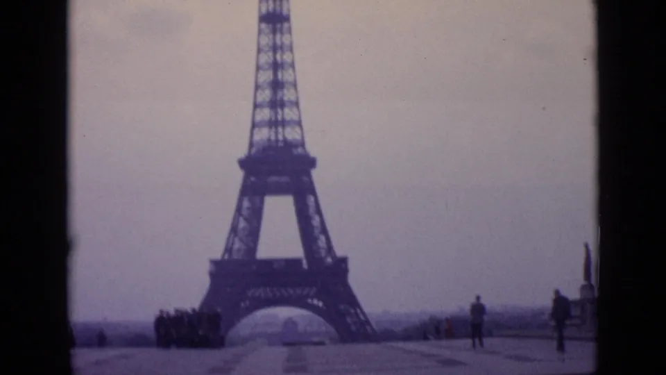1962 Paris frame showing the Eiffel Tower through or beside a car-window divider, with small pedestrians at the base.
