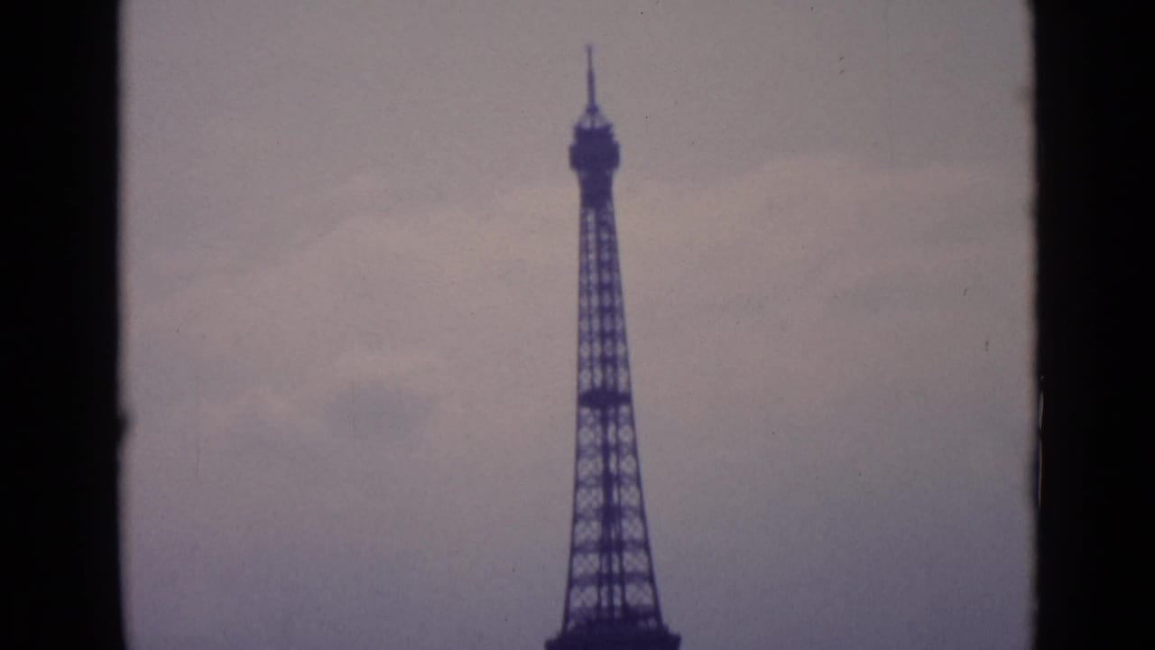 1962 Paris home-movie frame showing the Eiffel Tower rising into an overcast sky, cropped by dark 8mm frame edges.