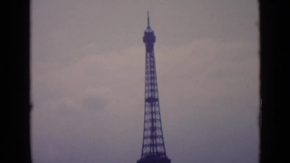 1962 Paris home-movie frame showing the Eiffel Tower rising into an overcast sky, cropped by dark 8mm frame edges.