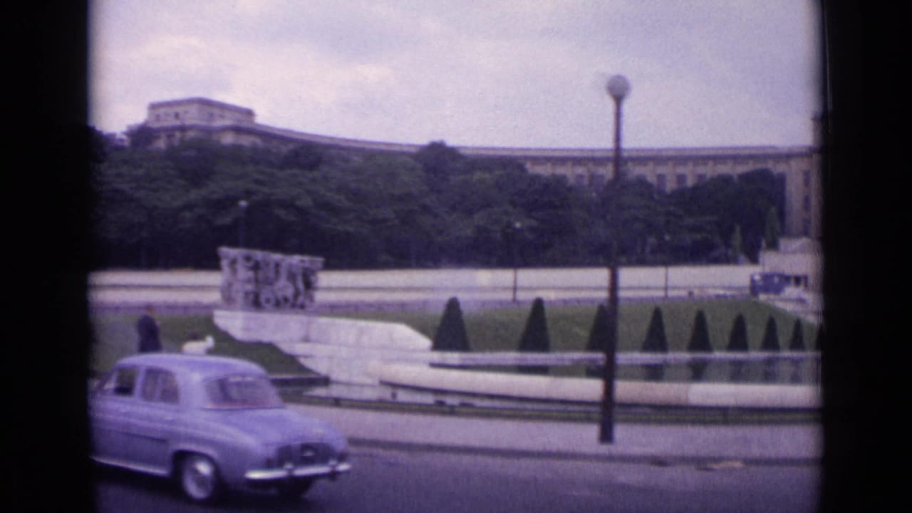 1962 Paris street view with a classic car passing the Trocadero gardens, fountain area, streetlamp, and Palais de Chaillot in the background.