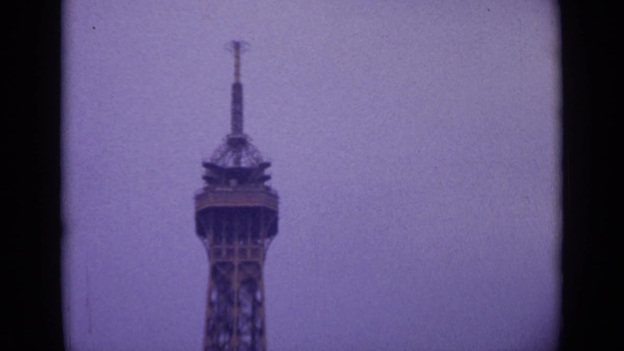 1962 Paris 8mm frame showing the upper section of the Eiffel Tower rising into a hazy sky, framed by dark film gate edges.