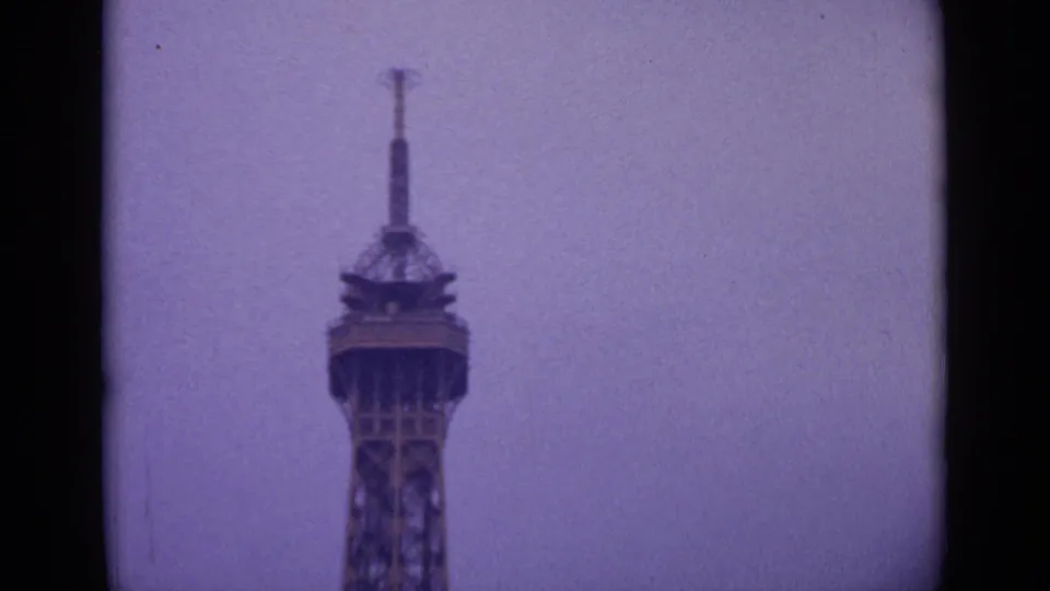 1962 Paris 8mm frame showing the upper section of the Eiffel Tower rising into a hazy sky, framed by dark film gate edges.