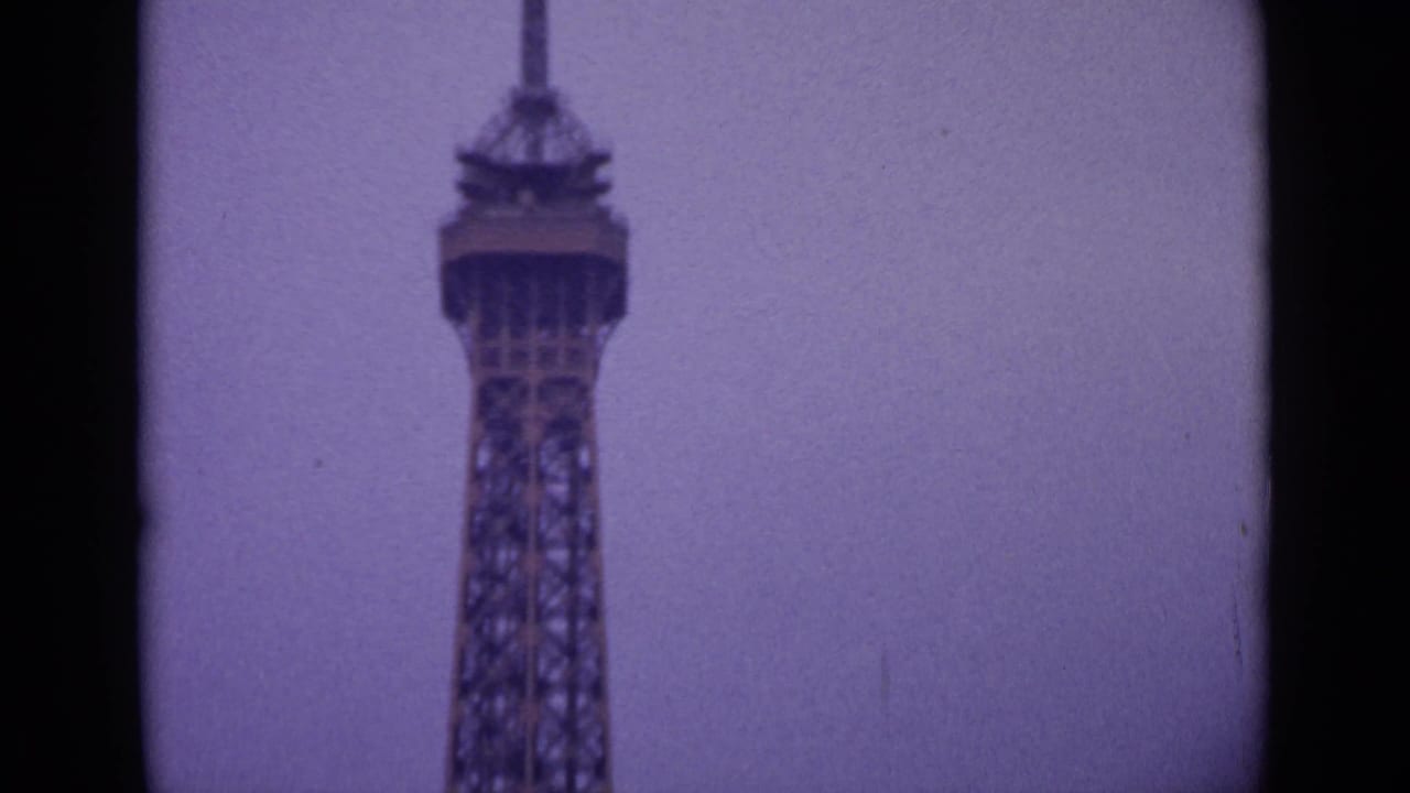 Upper section of the Eiffel Tower against a muted cloudy sky.