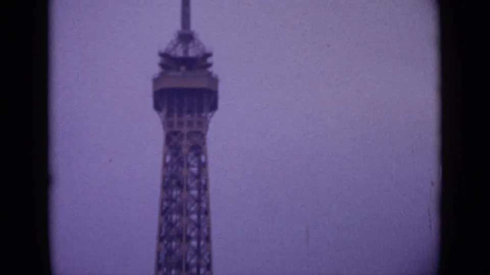 1962 8mm view of the Eiffel Tower's upper structure in Paris, framed with dark film edges and soft purple tint.